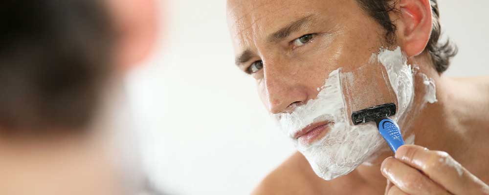 Man looking in the mirror, preparing for a wet shave with a razor.
